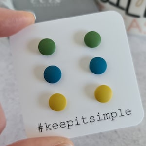 Könnte beinhalten: Ein Set mit sechs kleinen, runden, bunten Ohrringen. Die Ohrringe sind grün, blau und gelb. Die Ohrringe werden auf einer weißen Karte mit dem Text "#keepitsimple" präsentiert.