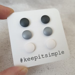 Può includere: Un set di sei orecchini a perno in tre colori: nero, argento e bianco. Gli orecchini sono esposti su una carta bianca con il testo "#keepitsimple".
