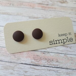 K&ouml;nnte beinhalten: Ein Paar braune Ohrstecker auf einer wei&szlig;en Karte mit dem Text "keep it simple".