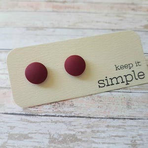 May include: Two small, round, maroon-colored stud earrings on a white card with the text "keep it simple".