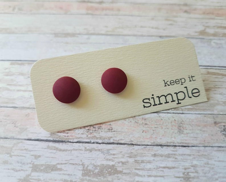 May include: Two small, round, maroon-colored stud earrings on a white card with the text "keep it simple".