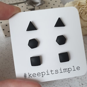 May include: A set of six black stud earrings in the shapes of a triangle, hexagon, and square. The earrings are displayed on a white card with the text "#keepitsimple".