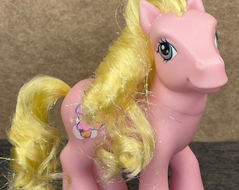 May include: Pink My Little Pony with a yellow glittery mane and tail. The pony has a cupcake symbol on its flank.