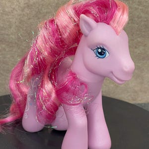 May include: A pink My Little Pony toy with long, pink and white hair with glitter. The pony has blue eyes and a pink body.