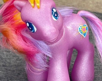 May include: A purple pony with a yellow, pink, and purple mane and tail. The pony has a blue heart with a sun inside on its side and a pink heart on its hoof.