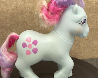 Peut inclure: Un poney jouet bleu clair avec une crinière et une queue roses et violettes. Le poney a un motif de fleur sur le côté et des yeux violets. Le jouet est un objet de collection vintage.