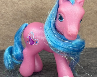 May include: A pink My Little Pony with blue iridescent hair. The pony has a purple and blue heart-shaped symbol on its flank and a white heart on its rear leg.