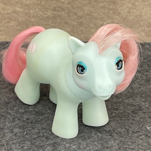 Puede incluir: Un juguete My Little Pony azul claro con pelo rosa y ojos azules. El pony tiene un corazón rosa en un lado.