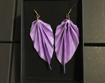 Può includere: Un paio di orecchini a forma di foglia di origami viola con ganci dorati, presentati in una scatola nera.