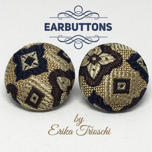 May include: A pair of gold, brown, and blue patterned fabric ear buttons. The ear buttons are round and have a geometric design.