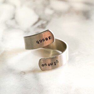Peut inclure: Une bague en argent avec les mots "queer enough" gravés dessus.