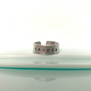 May include: A silver adjustable ring with the name "EARPER" engraved on it.