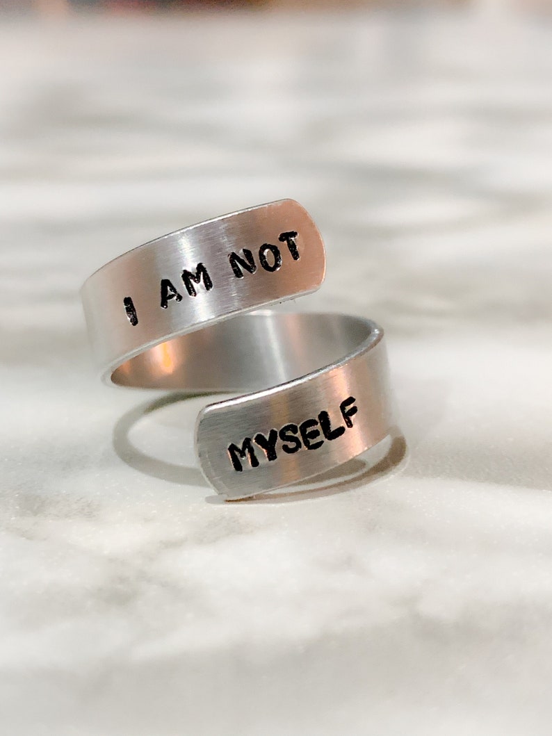 wrap style silver coloured ring with the words "i am not" on the top band and "myself" on the bottom band. Words are coloured black.