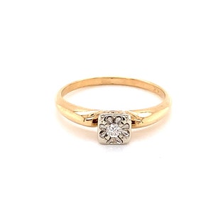 May include: A gold band ring with a single, small, square-shaped diamond in the center.