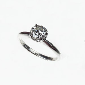 May include: A silver solitaire engagement ring with a round brilliant cut diamond.