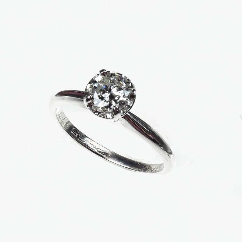 May include: A silver solitaire engagement ring with a round brilliant cut diamond.