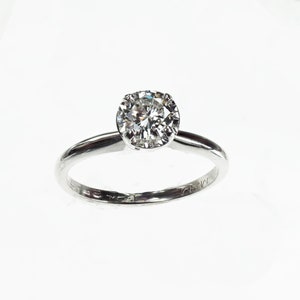 May include: A silver solitaire engagement ring with a round brilliant cut diamond.