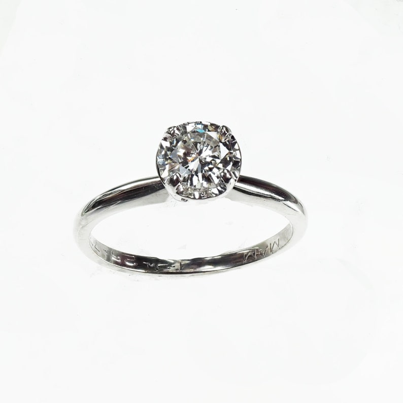 May include: A silver solitaire engagement ring with a round brilliant cut diamond.