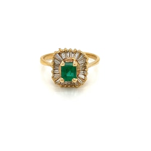 May include: A gold ring with a green emerald gemstone surrounded by a halo of baguette-cut diamonds.