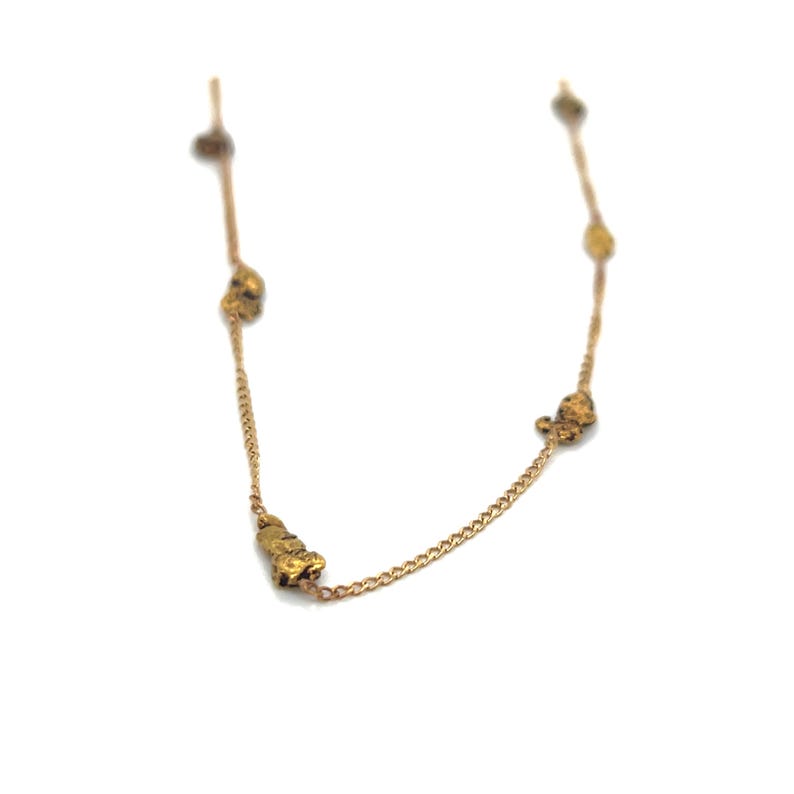 May include: A delicate gold-colored necklace featuring several irregularly shaped gold nuggets. The chain is fine and links the nuggets together. The necklace is displayed against a white background, highlighting the jewelry's details.