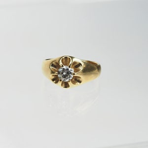 May include: A gold ring with a flower-shaped setting and a clear round gemstone in the centre.