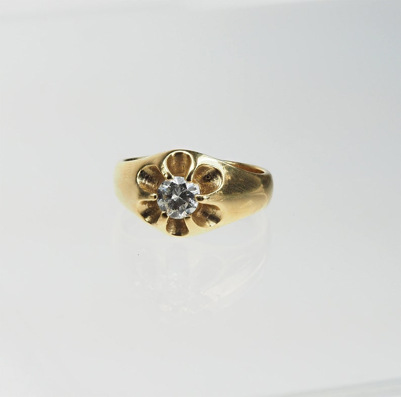 May include: A gold ring with a flower-shaped setting and a clear round gemstone in the centre.