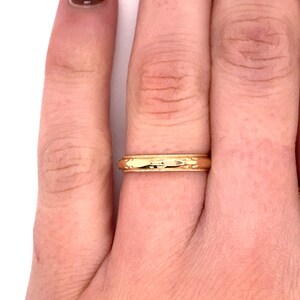 May include: A gold wedding band with a textured design. The band is worn on a finger.