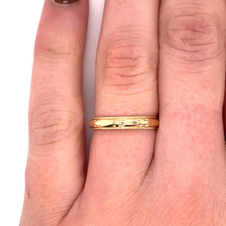 May include: A gold wedding band with a textured design. The band is worn on a finger.