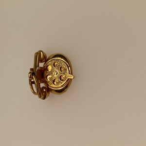 May include: A gold-colored charm in the shape of a rotary phone. The charm has a detailed design and is perfect for adding a vintage touch to a bracelet or necklace.