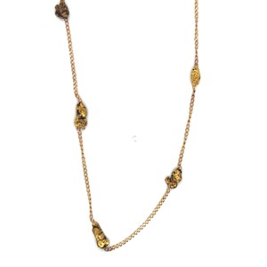 May include: A gold-colored necklace featuring several irregularly shaped gold nuggets strung along a delicate chain. The nuggets have a textured, organic appearance, and the chain has a subtle shine. The necklace is displayed against a white background.