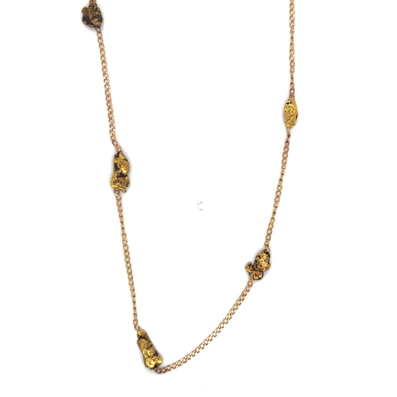 May include: A gold-colored necklace featuring several irregularly shaped gold nuggets strung along a delicate chain. The nuggets have a textured, organic appearance, and the chain has a subtle shine. The necklace is displayed against a white background.