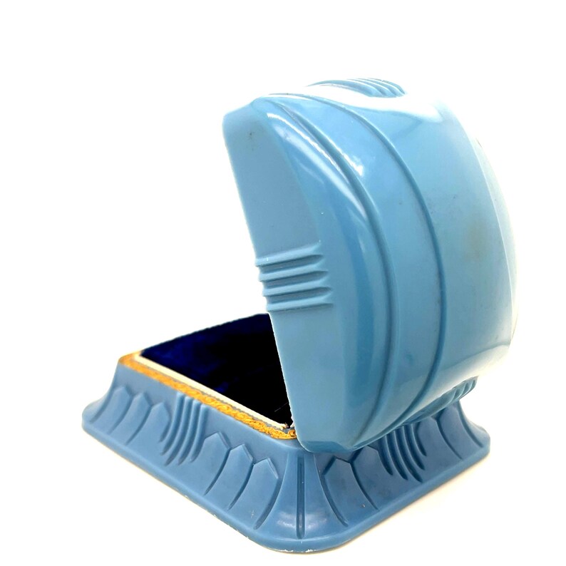 May include: A vintage, light blue jewelry box with an open lid. The box has a geometric design with a gold-colored trim around the interior. The inside of the box is lined with dark blue velvet.