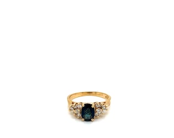 May include: A gold ring featuring a dark blue oval gemstone at the center, flanked by smaller clear gemstones. The ring has a classic design with a polished finish, set against a white background.