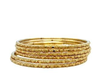 May include: Six gold bangles are stacked together. Each bangle features a repeating pattern of small, raised dots. The bangles are circular and display an intricate design. The jewellery is set against a white background.