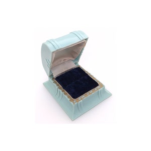 May include: A light blue ring box with a gold trim and a dark blue velvet interior.