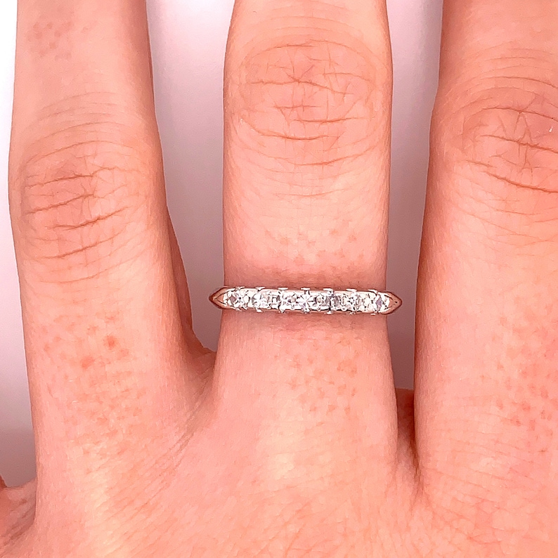 May include: A thin silver band with a row of small, clear diamonds set in a prong setting.