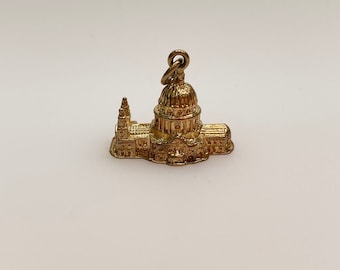 May include: A gold charm in the shape of St. Paul's Cathedral in London. The charm is detailed and has a loop for attaching to a necklace or bracelet.