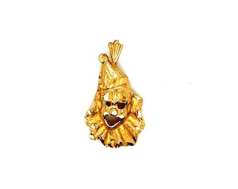 May include: A gold-colored pendant charm in the shape of a clown's face. The charm has a detailed design with a textured surface.