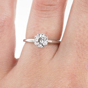 May include: A simple solitaire engagement ring with a round brilliant cut diamond set in a white gold band.