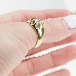 May include: A gold ring featuring a single round diamond set in an intricate, openwork design.