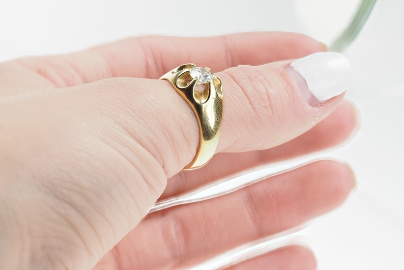 May include: A gold ring featuring a single round diamond set in an intricate, openwork design.