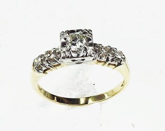 May include: A gold and silver engagement ring with a single round diamond and smaller diamonds set in the band.