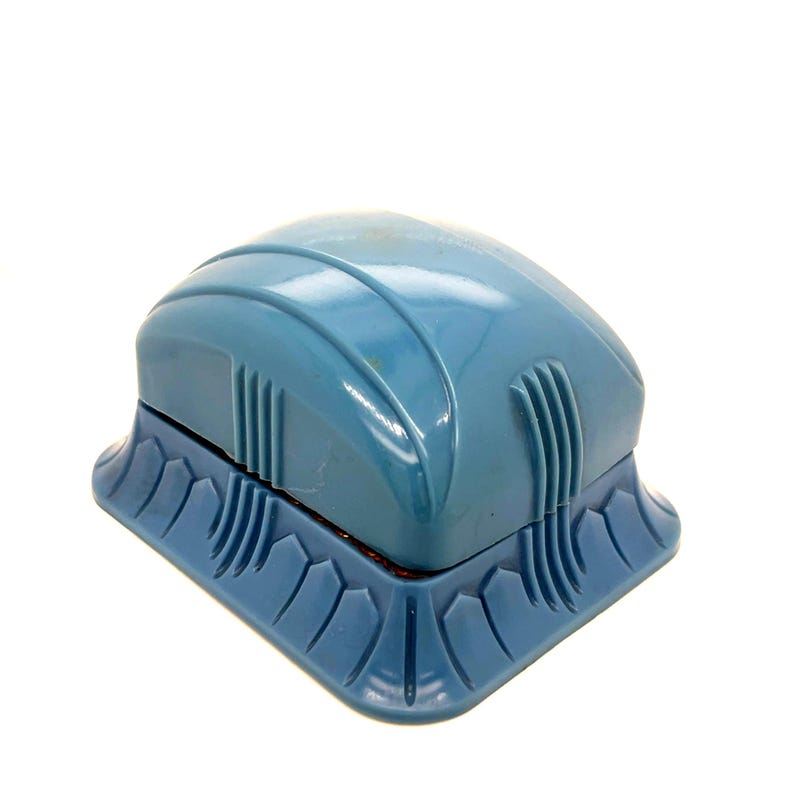 May include: A vintage, light blue magnetic aquarium cleaner. The cleaner has a rounded top with vertical ridges and a decorative base. The base has a repeating pattern of curved shapes. The cleaner is designed to clean the inside and outside of an aquarium.