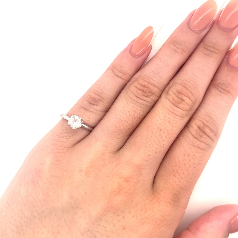 May include: A simple solitaire engagement ring with a round brilliant cut diamond set in a white gold band.