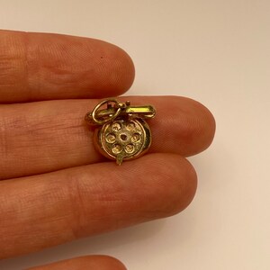 May include: A gold charm in the shape of a rotary phone. The charm is detailed with a dial and a handset.