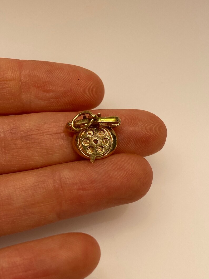 May include: A gold charm in the shape of a rotary phone. The charm is detailed with a dial and a handset.