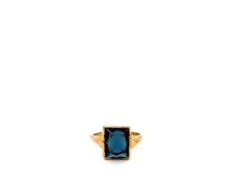 May include: A gold-colored ring featuring a large, rectangular, dark blue gemstone. The ring has a simple band that widens slightly at the shoulders, leading to the rectangular setting. The gemstone is the focal point, set in a gold frame.