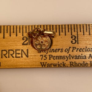 May include: Gold charm of a rotary phone with a gold chain. The charm is about 1 inch in diameter. The charm is marked "Refiners of Precious Metals, 75 Pennsylvania Ave, Warwick, Rhode Island".