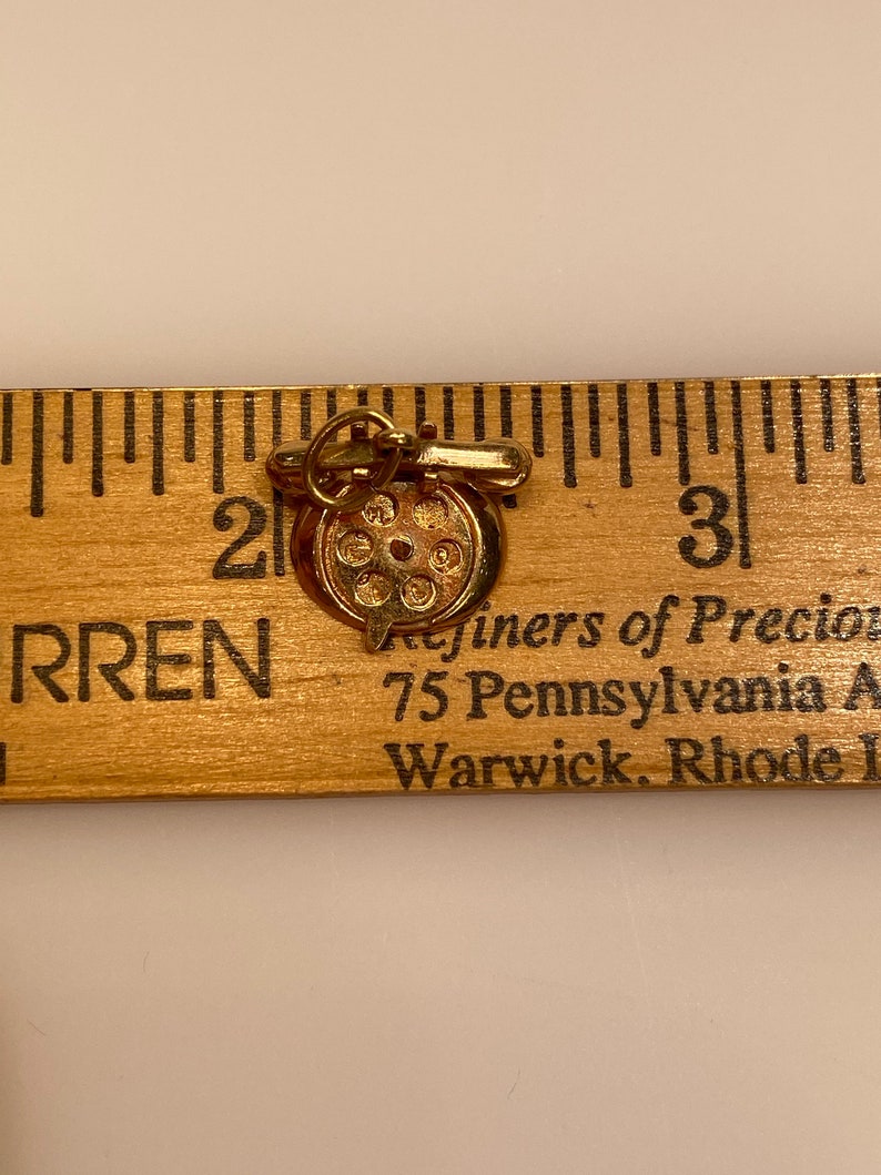 May include: Gold charm of a rotary phone with a gold chain. The charm is about 1 inch in diameter. The charm is marked "Refiners of Precious Metals, 75 Pennsylvania Ave, Warwick, Rhode Island".