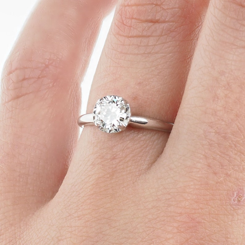 May include: A silver engagement ring with a round, clear diamond set in a halo setting.